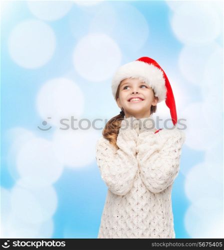 christmas, holidays, childhood and people concept - smiling girl in santa helper hat over blue lights background