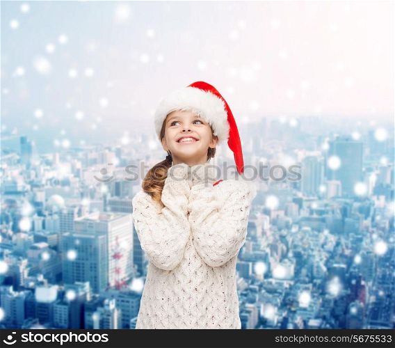 christmas, holidays, childhood and people concept - smiling girl in santa helper hat over snowy city background