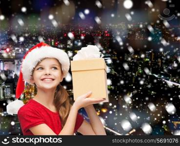 christmas, holidays, childhood and people concept - smiling girl in santa helper hat with gift box over snowy night city background