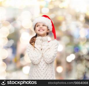 christmas, holidays, childhood and people concept - smiling girl in santa helper hat over lights background