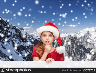 christmas, holidays, childhood and people concept - smiling little girl in santa helper hat with finger on her lips over snowy mountains background