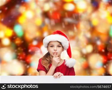 christmas, holidays, childhood and people concept - smiling little girl in santa helper hat with finger on her lips over red lights background