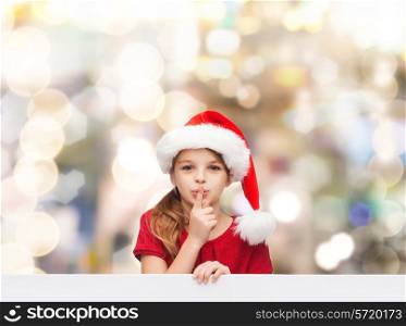 christmas, holidays, childhood and people concept - smiling little girl in santa helper hat with finger on her lips over lights background
