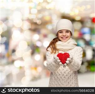 christmas, holidays, childhood, presents and people concept - dreaming girl in winter clothes with red heart over lights background