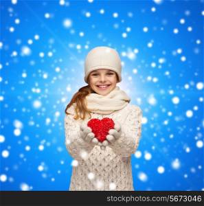 christmas, holidays, childhood, presents and people concept - dreaming girl in winter clothes with red heart over blue snowing background