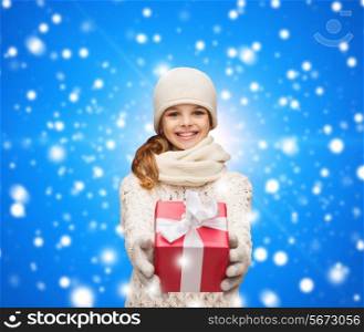 christmas, holidays, childhood, presents and people concept - dreaming girl in winter clothes with gift box over blue snowing background