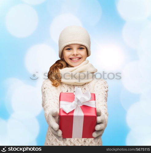 christmas, holidays, childhood, presents and people concept - dreaming girl in winter clothes with gift box over blue lights background