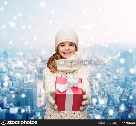 christmas, holidays, childhood, presents and people concept - dreaming girl in winter clothes with gift box over snowy city background