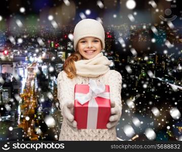 christmas, holidays, childhood, presents and people concept - dreaming girl in winter clothes with gift box over snowy city background