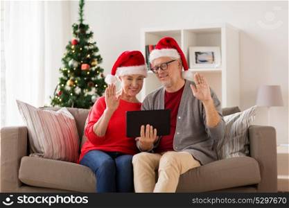 christmas, holidays, communication and people concept - happy smiling senior couple in santa hats with tablet pc computer having video chat at home. happy senior couple with tablet pc at christmas
