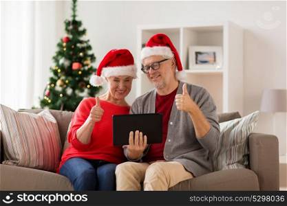 christmas, holidays, communication and people concept - happy smiling senior couple in santa hats with tablet pc computer having video chat at home. happy senior couple with tablet pc at christmas