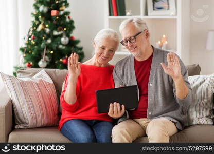 christmas, holidays, communication and people concept - happy smiling senior couple with tablet pc computer having video chat and waving hands at home. happy senior couple with tablet pc at christmas