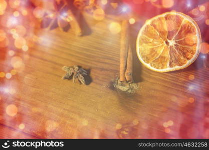 christmas, holidays, cooking and spice concept - close up of cinnamon, anise and dried orange on wooden board over lights