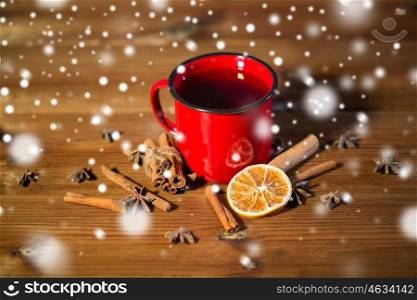 christmas, holidays, cooking and spice concept - close up of tea cup with cinnamon, anise and dried orange on wooden table from top