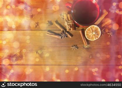 christmas, holidays, cooking and spice concept - close up of tea cup with cinnamon, anise and dried orange on wooden table from top over lights