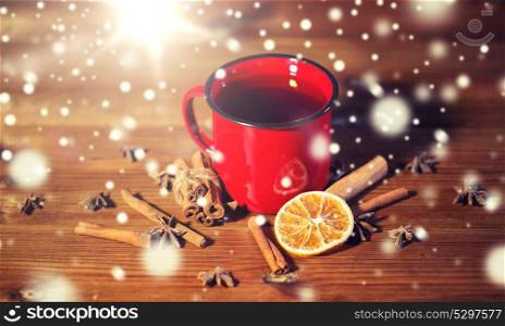 christmas, holidays, cooking and spice concept - close up of tea cup with cinnamon, anise and dried orange on wooden table from top. close up of tea cup with spices on wooden table