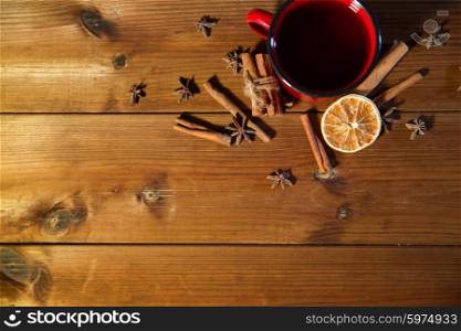 christmas, holidays, cooking and spice concept - close up of tea cup with cinnamon, anise and dried orange on wooden table from top