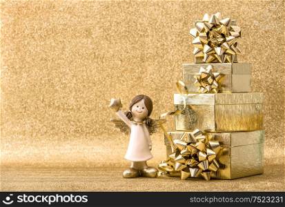 Christmas holidays decoration. Gift boxes and little angel on bright golden background
