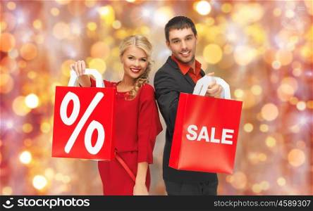 christmas, holidays, discount and people concept - couple with sale and percentage sign on red shopping bags over lights background