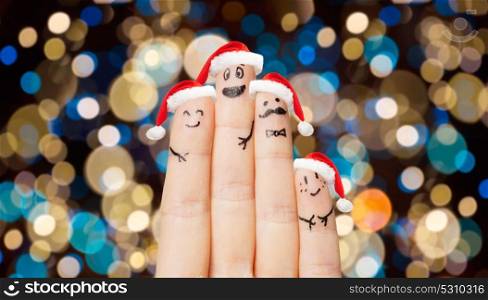 christmas, holidays, family and body parts concept - close up of four fingers with smiles in santa hats over lights background. close up of fingers in santa hats at christmas