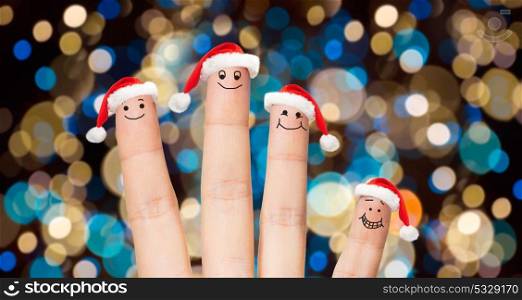 christmas, holidays, family and body parts concept - close up of four fingers with smiles in santa hats over lights background. close up of fingers in santa hats at christmas