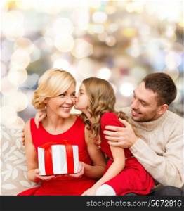 christmas, holidays, family and people concept - happy mother, father and little girl with gift box kissing over lights background