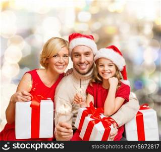 christmas, holidays, family and people concept - happy mother, father and little girl in santa helper hats with gift boxes over lights background
