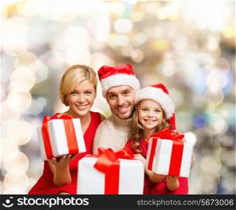 christmas, holidays, family and people concept - happy mother, father and little girl in santa helper hats with gift boxes over lights background