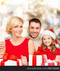 christmas, holidays, family and people concept - happy mother, father and little girl in santa helper hat with gift boxes over lights background