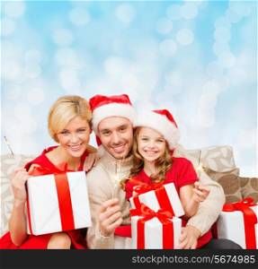 christmas, holidays, family and people concept - happy mother, father and little girl in santa helper hats with gift boxes and sparklers over blue lights background