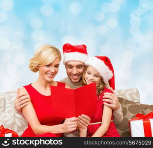 christmas, holidays, family and people concept - happy mother, father and little girl in santa helper hats with gift boxes reading geeting card over blue lights background