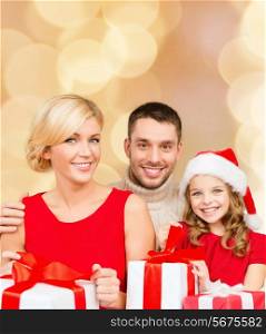 christmas, holidays, family and people concept - happy mother, father and little girl in santa helper hat with gift boxes over beige lights background