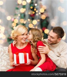 christmas, holidays, family and people concept - happy mother, father and little girl with gift box kissing over living room and christmas tree background