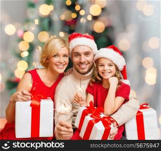 christmas, holidays, family and people concept - happy mother, father and little girl in santa helper hats with gift boxes over living room and christmas tree background