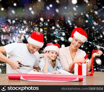 christmas, holidays, family and people concept - happy mother, father and little girl in santa helper hats with gift box and scissors over snowy night city background