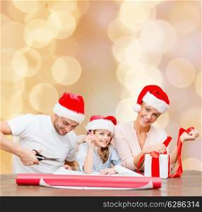 christmas, holidays, family and people concept - happy mother, father and little girl in santa helper hats with gift box and scissors over beige lights background