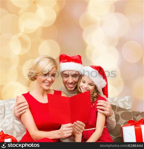 christmas, holidays, family and people concept - happy mother, father and little girl in santa helper hats with gift boxes reading geeting card over beige lights background