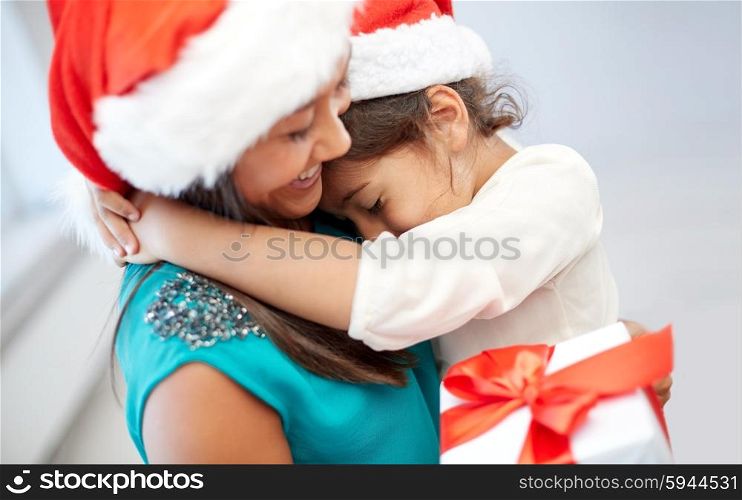 christmas, holidays, family, childhood and people concept - happy mother and little girl in santa hats cuddling at home