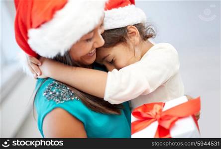 christmas, holidays, family, childhood and people concept - happy mother and little girl in santa hats cuddling at home