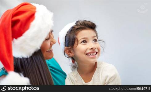 christmas, holidays, family, childhood and people concept - happy mother and little girl in santa hats at home