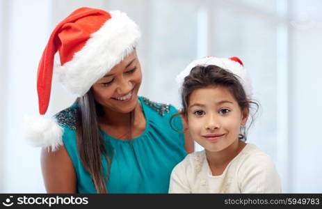 christmas, holidays, family, childhood and people concept - happy mother and little girl in santa hats at home