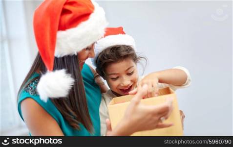 christmas, holidays, family, childhood and people concept - happy mother and little girl in santa hats opening gift box at home