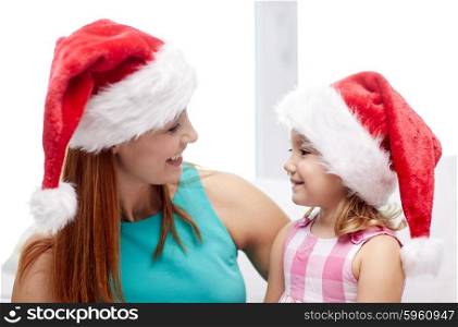 christmas, holidays, family, childhood and people concept - happy mother and little girl in santa hats at home