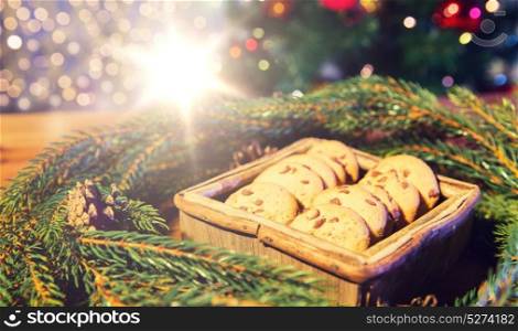 christmas, holidays, food and baking concept - close up of natural green fir christmas wreath and oat cookies in wooden box on table over lights. natural green fir christmas wreath and oat cookies