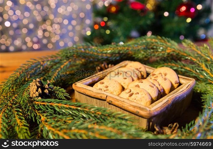 christmas, holidays, food and baking concept - close up of natural green fir christmas wreath and oat cookies in wooden box on table over lights