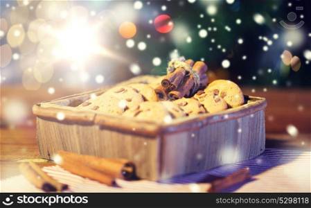 christmas, holidays, food and baking concept - close up of oat cookies in wooden box and cinnamon on table over lights. close up of christmas oat cookies on wooden table