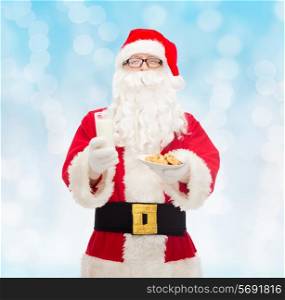 christmas, holidays, food, drink and people concept - man in costume of santa claus with glass of milk and cookies over blue lights background