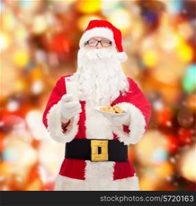 christmas, holidays, food, drink and people concept - man in costume of santa claus with glass of milk and cookies over red lights background