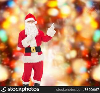 christmas, holidays, gesture and people concept - man in costume of santa claus pointing fingers over red lights background