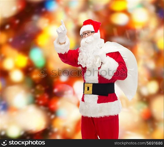 christmas, holidays, gesture and people concept - man in costume of santa claus with bag pointing finger up over red lights background